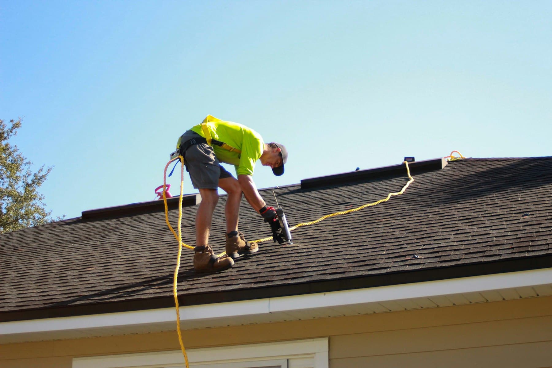 Roofer in a safety harness fastening shingles on a residential roof